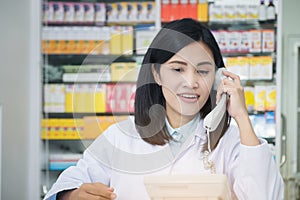 Pharmacy worker talking by phone, Attractive young smiling female at desk with telephone to ear