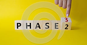 From Phase 2 to 3 symbol. Businessman Hand points at wooden cubes with words Phase 2 and Phase 3. Beautiful yellow background.