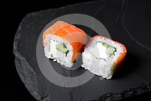 Philadelphia roll sushi with salmon on a dark background. Two pieces of philadelphia sushi roll close up on a stone Board