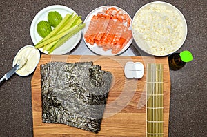 philadelphia sushi maki and ingredients, on a wooden cutting board, top view, copy space on nori sheet
