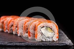 Philadelphia sushi rolls with salmon and cream cheese and avocado on a black slate plate close up