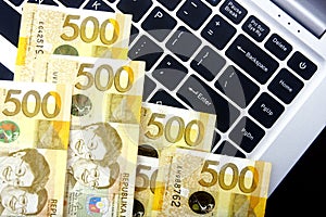 Philippine peso bills on a laptop computer.