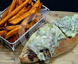 Philly cheese steak sandwich and fries on a wood board