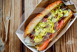 Philly cheese steak sandwich with meat, vegetables, cheese and sause in box on wooden table