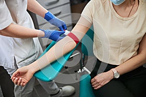 Phlebotomy technician tightening the elastic band on the patient arm