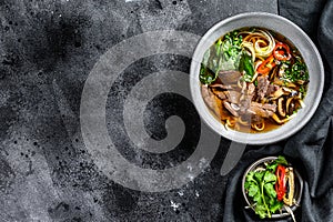 Pho Bo Vietnamese fresh rice noodle soup with beef, herbs and chili. Black background. Top view. Copy space