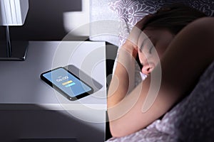 Phone alarm waking up tired sleeping woman in bed at night or morning. Cellphone on table with clock timer and snooze button. photo