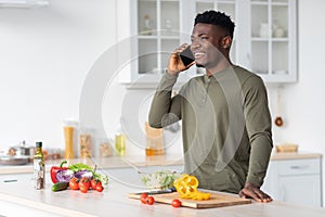 Phone Call. Handsome Young Black Guy Talking On Cellphone In Kitchen Interior