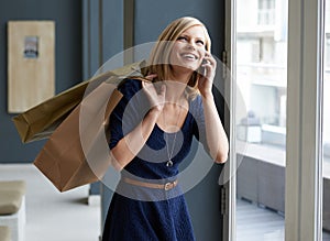 Phone call, shopping bags and young woman by window of retail fashion store or boutique. Happy, smile and female person