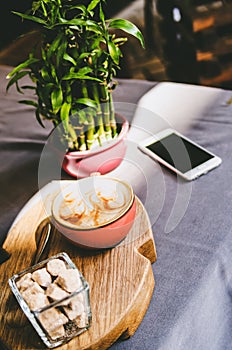 The phone, cappuccino, brown sugar and a vase with bamboo stand on the table.