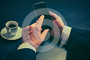 Phone and a cup of coffee in the hands of a businessman in dark colors