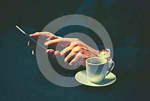 Phone and a cup of coffee in the hands of a businessman in dark colors