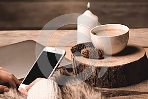 Phone in the hands of the girl, a white cup with coffee, candle and cones