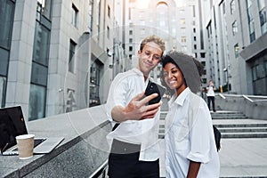 With phone in hands. Man with afrian american woman together in the city outdoors