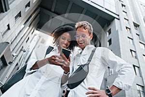 With phone in hands. Man with afrian american woman together in the city outdoors