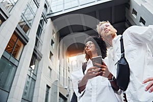 With phone in hands. Man with afrian american woman together in the city outdoors