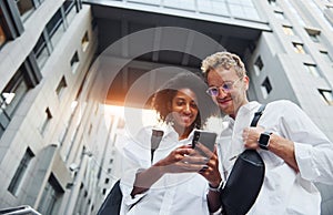 With phone in hands. Man with afrian american woman together in the city outdoors