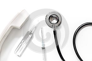 Phone handset, phonendoscope, syringe and ampoule on isolated white background top view call doctor