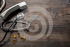 Phone handset, pills and phonendoscope on dark wooden desk top view make appointment with a doctor space for text