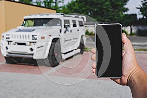 The phone is in the man`s hand. Against the background of a white SUV. Online purchase, car rental. The concept of road transport