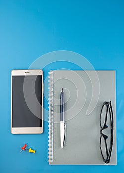 Phone, notebook and pen, glasses buttons lie on a blue background