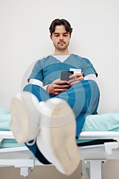 Phone, nurse and man on bed to relax in hospital, typing email on break and telehealth. Smartphone, serious medical