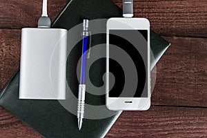 Phone and power bank connected by cord with pen and notebook on