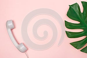 Phone receiver and Monstera palm leaf on pink background