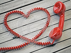 Phone reciever and cord as heart on white wooden background. Love hotline concept. 3d