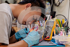 Phone repair concept a young electrical technician using an ammeter measuring the current in a circuit of an electronic device