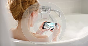 Phone, social media and woman relax in bath with bubbles, candles and self care in home. Scroll, online and person swipe