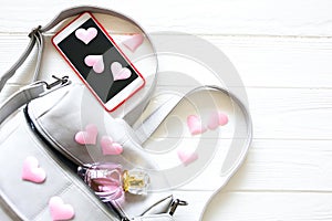 Phone, stylish bag and perfumes on white background. Beautiful flat lay with hearts. The best present for the girl. Woman`s or