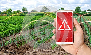 A phone warns of the danger on background of a farm plantation field. Monitoring and analysis of the presence of chemicals