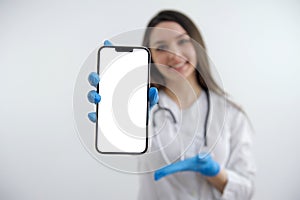 phone with a white screen girl doctor shows a hand in blue gloves on an empty space For text white background Your