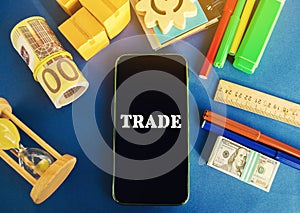 Phone with the word Trade on a blue background with money, boxes and hourglass. Business market and finance concept. Transfer of