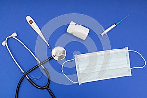 Phonendoscope, protective medical face mask and electronical thermometer on blue background