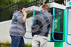 Phoning home. Two young men making phone calls from public pay-phone booths.