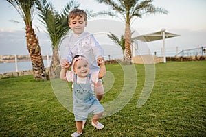 Photo of a 7-year blond boy walking with his little sister in the garden of a resort in a tropical destination