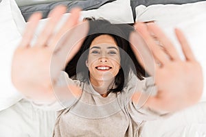 Photo from above of happy woman 30s, smiling while lying in bed at home
