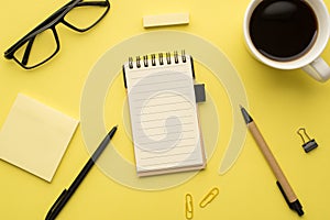 Photo above of notebook pen paperclips notes cup of coffee and glasses isolated on the yellow background