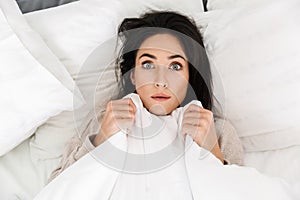 Photo from above of shocked woman 30s lying in bed at home, under white blanket