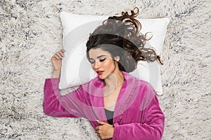 Photo from above of young woman wearing girlish housecoat lying and sleeping on white fur in apartment photo