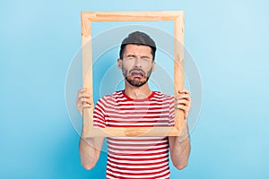 Photo of abused sad young man dressed striped t-shirt holding brown frame crying isolated blue color background