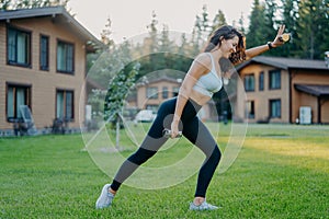 Photo of active slim woman does sport exercises with dumbbells, dressed in cropped top, leggings, sneakers, leads active lifestye photo