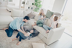 Photo of adopted family four members spend leisure time rejoicing pillows fight giggle sit couch living room