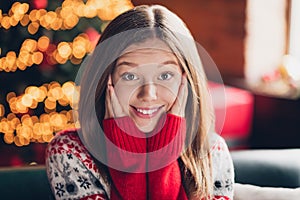 Photo of adorable cheerful girl toothy smile arms touch cheeks enjoy festive magic time house indoors