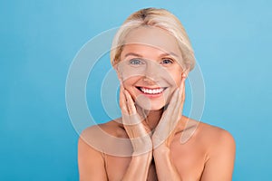 Photo of adorable cheerful senior woman nude shoulders arms touching cheeks enjoying soft skin empty space isolated blue