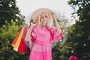 Photo of adorable cute lady pensioner dressed pink clothes arm hand headwear walking holding shopping bags smiling