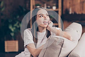 Photo of adorable dreamy young woman white t-shirt sitting couch arm cheek looking window smiling indoors apartment room