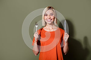 Photo of adorable hungry young girl wear orange t shirt hold spoon knife delicious food in cafeteria  on khaki